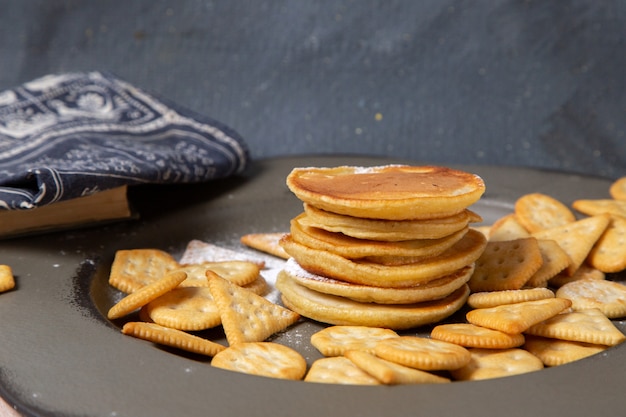 Vista frontal de deliciosos panqueques con galletas en la superficie gris