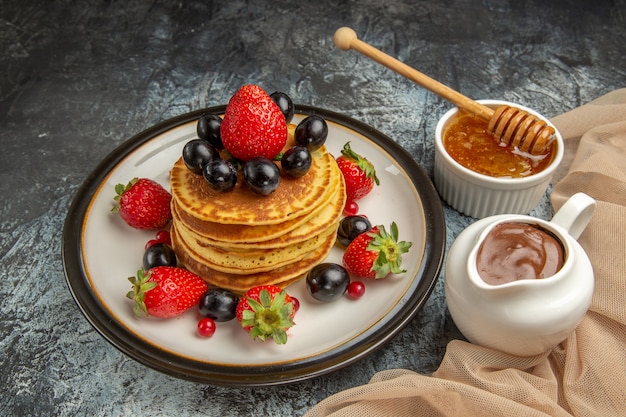 Vista frontal deliciosos panqueques con miel y frutas en la superficie de la luz pastel de frutas dulces