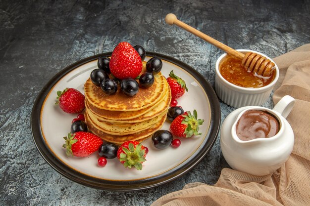 Vista frontal deliciosos panqueques con miel y frutas en la superficie de la luz pastel de frutas dulces