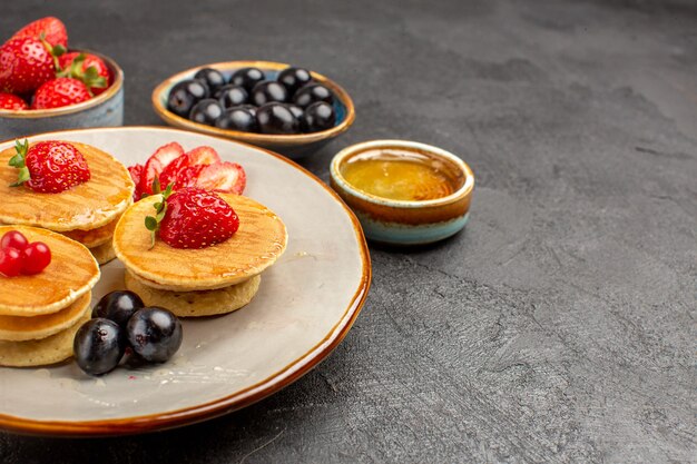 Vista frontal deliciosos panqueques poco formados con frutas sobre una superficie gris pastel pastel de frutas