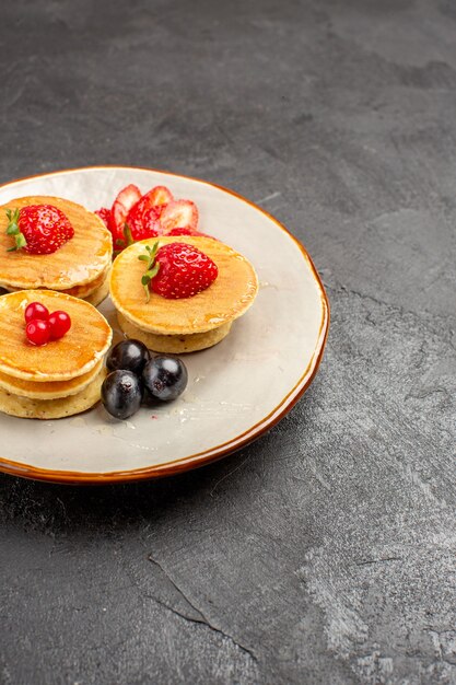 Vista frontal deliciosos panqueques poco formados con frutas en la superficie gris pastel de frutas pastel