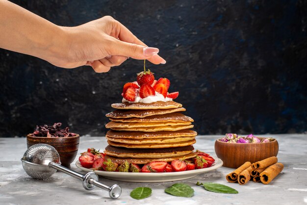 Una vista frontal deliciosos panqueques redondos con crema y fresas rojas en la mesa de luz pastel de frutas