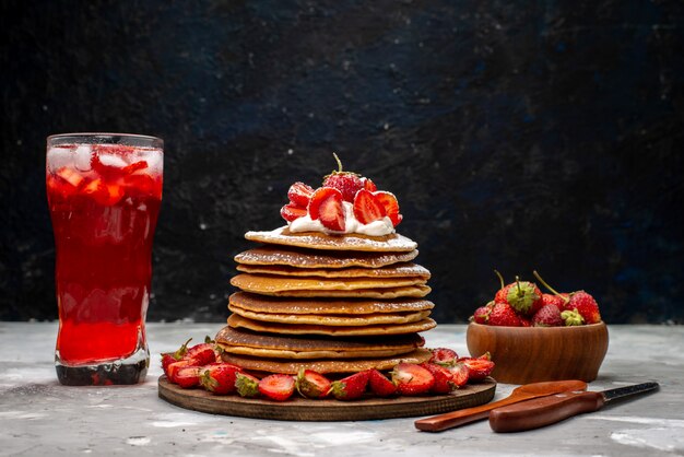 Una vista frontal deliciosos panqueques redondos con fresas rojas frescas y cóctel de fresa en el pastel de escritorio ligero