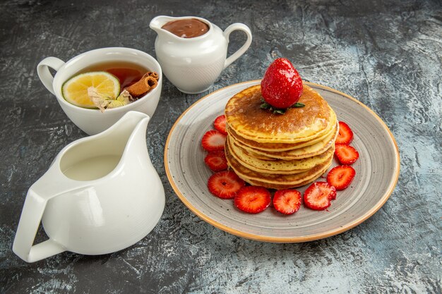 Vista frontal deliciosos panqueques con taza de té y frutas en superficie ligera pastel de frutas dulce