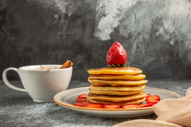 Vista frontal deliciosos panqueques con taza de té y frutas en la superficie de la luz de la torta de frutas dulces