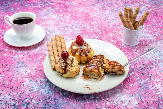 Vista frontal de deliciosos pasteles afrutados con crema y chocolate dentro de un plato blanco junto con café