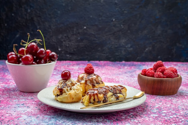 Vista frontal de deliciosos pasteles afrutados con crema y chocolate dentro de un plato blanco junto con frutas frescas