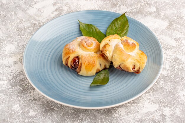 Vista frontal deliciosos pasteles afrutados dulces horneados con hojas verdes dentro de la placa azul sobre la superficie gris pastel pastelería dulce hornear té