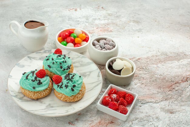 Vista frontal deliciosos pasteles con coloridos caramelos y galletas sobre fondo blanco pastel de postre pastel color arco iris caramelo