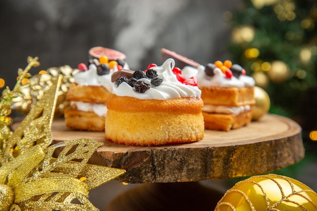 Vista frontal deliciosos pasteles de crema alrededor de los juguetes del árbol de año nuevo en el escritorio oscuro pastel de postre dulce foto crema