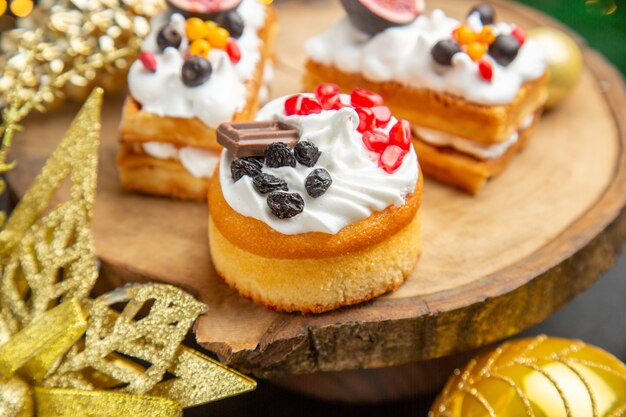 Vista frontal deliciosos pasteles de crema alrededor de juguetes de árbol de año nuevo sobre un fondo oscuro pastel de postre dulce foto crema
