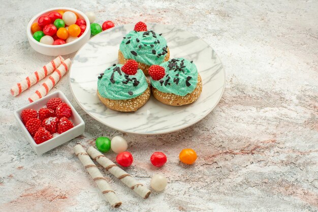 Vista frontal deliciosos pasteles de crema con caramelos de colores sobre fondo blanco pastel de galleta crema de postre dulce