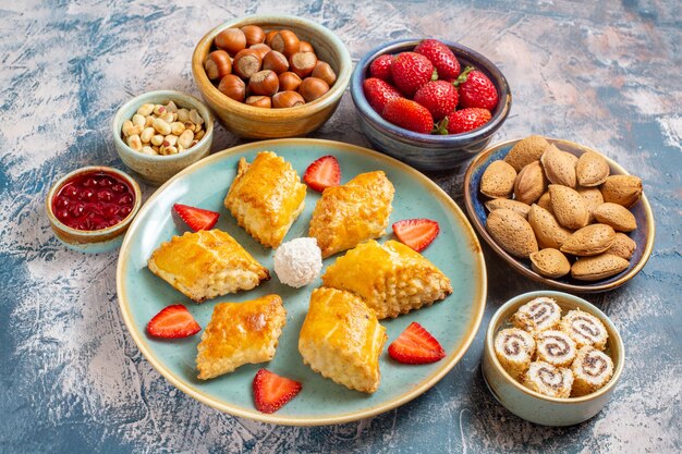 Vista frontal de deliciosos pasteles dulces con frutas y nueces sobre superficie azul