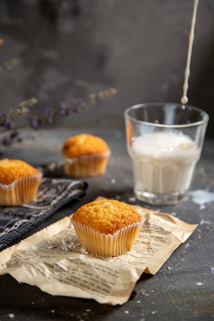 Una vista frontal deliciosos pasteles con flores púrpuras y leche en la mesa gris galleta té galleta dulce