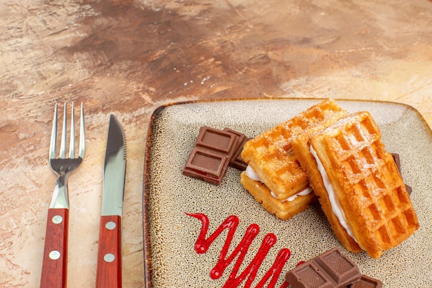 Vista frontal deliciosos pasteles de gofres con barras de chocolate en el piso marrón