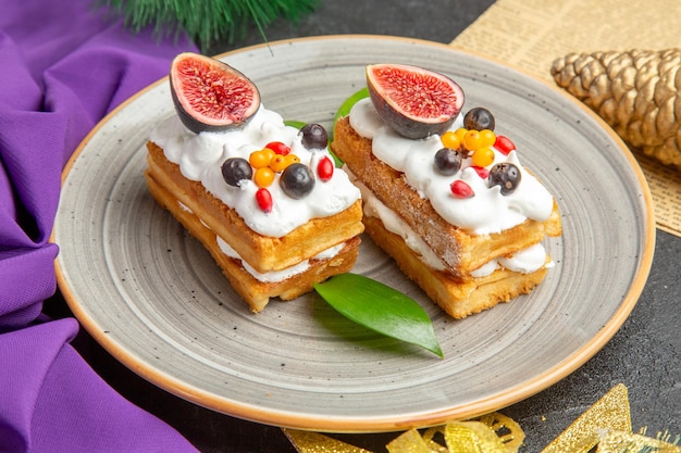 Vista frontal deliciosos pasteles de gofres con frutas alrededor de los juguetes del árbol de vacaciones sobre fondo oscuro