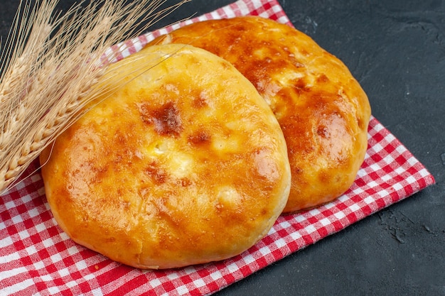 Vista frontal de deliciosos pasteles recién horneados sobre una toalla despojada de rojo y un pico en blackground oscuro