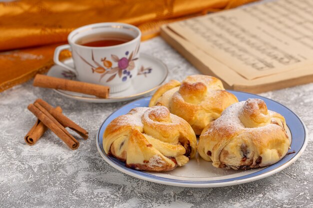 Vista frontal deliciosos pasteles con relleno dentro de la placa junto con té y canela en la mesa blanca, pastel de azúcar dulce hornear fruta de pastelería