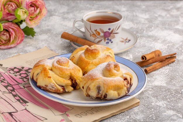 Vista frontal deliciosos pasteles con relleno dentro de la placa junto con té y canela en la mesa blanca, pastel de azúcar dulce hornear fruta de pastelería