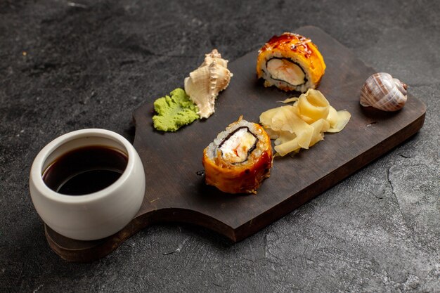 Vista frontal de deliciosos rollos de pescado de comida de sushi con salsa wassabi en pared gris