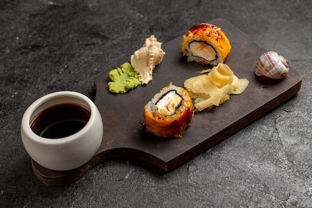 Vista frontal de deliciosos rollos de pescado de comida de sushi con salsa wassabi en pared gris