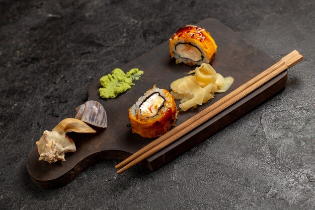 Vista frontal de deliciosos rollos de pescado de comida de sushi con salsa wassabi en pared gris