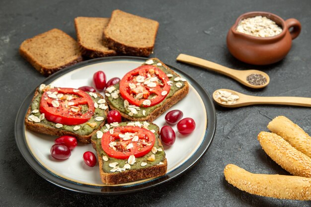 Vista frontal deliciosos sándwiches con pasta de aguacate y tomates dentro de la placa en el escritorio gris pan de sándwich de hamburguesa de bollo de bocadillo