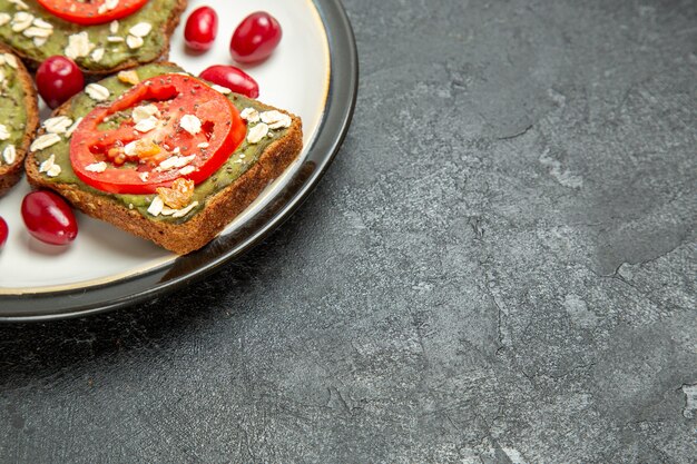 Vista frontal deliciosos sándwiches con pasta de aguacate y tomates dentro de la placa en el escritorio gris pan sándwich de hamburguesa pan de aperitivo