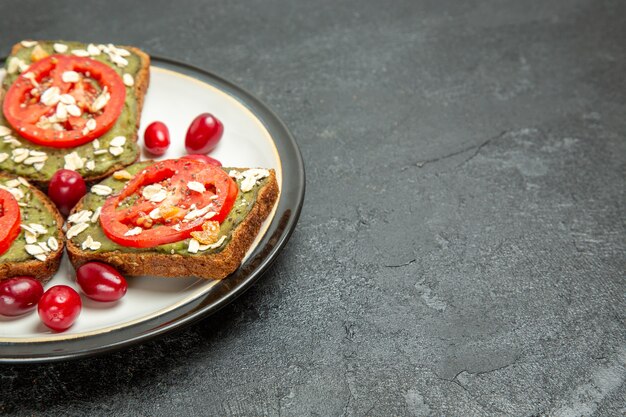 Vista frontal deliciosos sándwiches con pasta de aguacate y tomates dentro de la placa sobre el fondo gris pan sándwich de hamburguesa pan de aperitivo