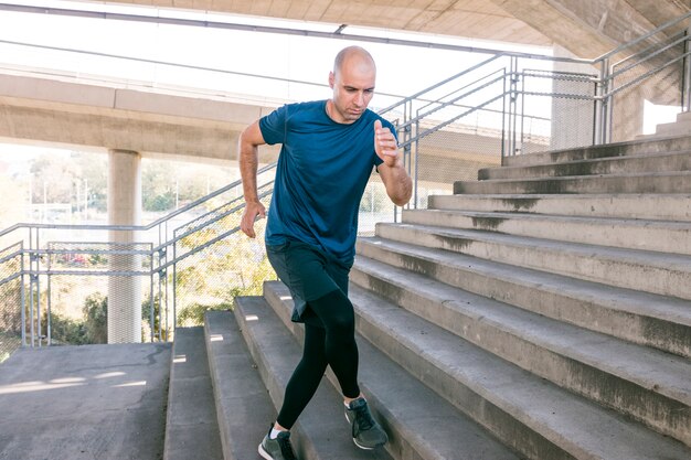 Vista frontal del deportista corredor masculino corriendo por las escaleras de la ciudad para trotar