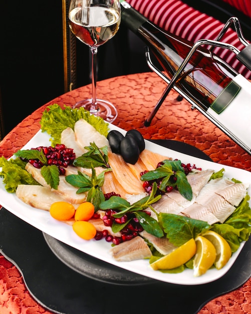 Una vista frontal diferentes comidas de mariscos dentro de un plato blanco junto con hojas verdes y limones en rodajas sobre la mesa