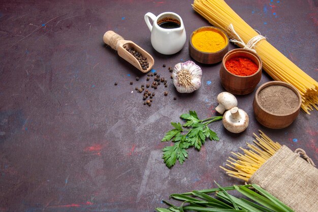 Vista frontal de diferentes condimentos con pasta cruda y champiñones en la superficie oscura del producto comida comida cruda