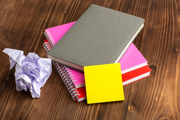 Vista frontal de diferentes cuadernos coloridos sobre la superficie marrón