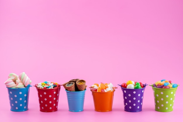 Una vista frontal de diferentes dulces como confituras, mermeladas, caramelos dentro de cestas en rosa, color dulce de azúcar