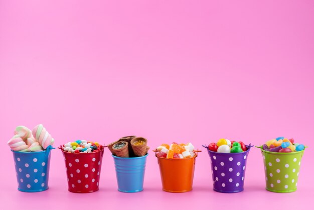 Una vista frontal de diferentes dulces como confituras, mermeladas, caramelos dentro de cestas en rosa, color dulce de azúcar