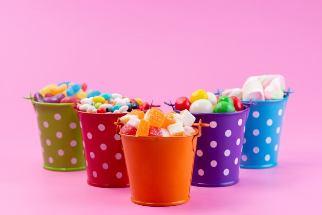 Una vista frontal de diferentes dulces como confituras, mermeladas, caramelos dentro de cestas en rosa, color dulce de azúcar