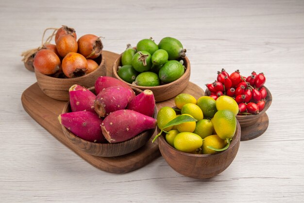 Vista frontal de diferentes frutas feijoas bayas y otras frutas dentro de placas sobre fondo blanco comida madura exótica foto color tropical