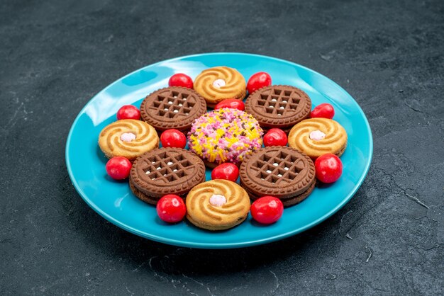 Vista frontal de diferentes galletas de azúcar dentro de la placa con caramelos sobre una superficie gris galletas de té dulce de azúcar dulces galletas