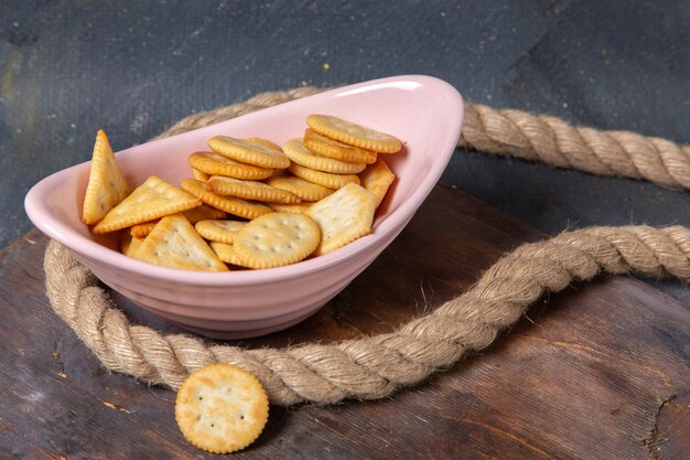 Vista frontal de diferentes galletas dentro de la placa rosa con cuerdas en la superficie gris