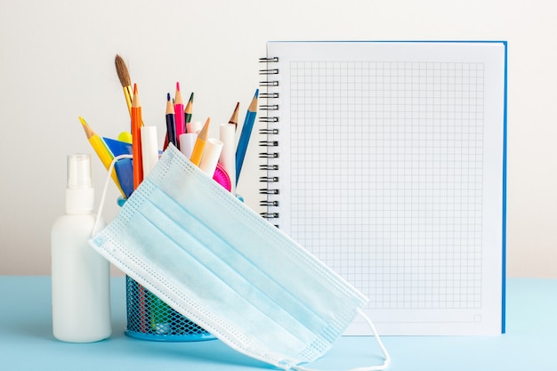 Vista frontal de diferentes lápices de colores con cuadernos y spray sobre escritorio azul