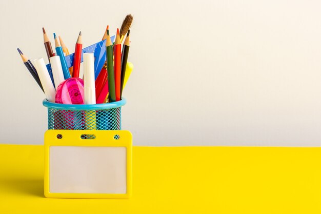 Vista frontal de diferentes lápices de colores con rotuladores en el escritorio amarillo claro