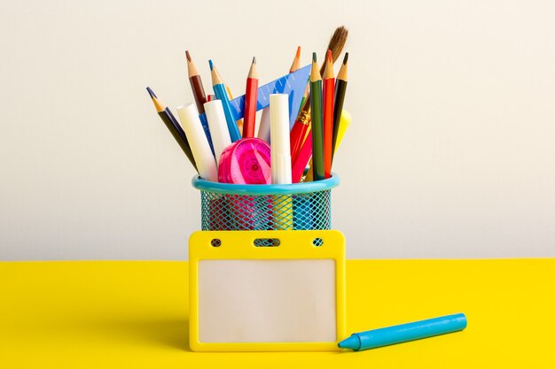 Vista frontal de diferentes lápices de colores con rotuladores en el escritorio amarillo