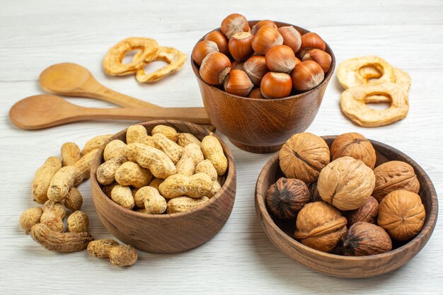 Vista frontal diferentes nueces cacahuetes avellanas y nueces sobre superficie blanca