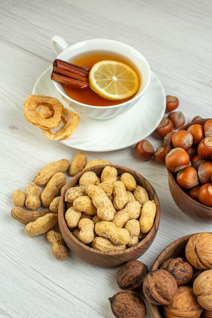 Vista frontal diferentes nueces cacahuetes avellanas y nueces con taza de té sobre superficie blanca