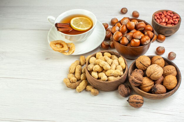 Vista frontal diferentes nueces cacahuetes avellanas y nueces con taza de té sobre superficie blanca