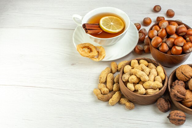 Vista frontal diferentes nueces cacahuetes avellanas y nueces con taza de té sobre superficie blanca