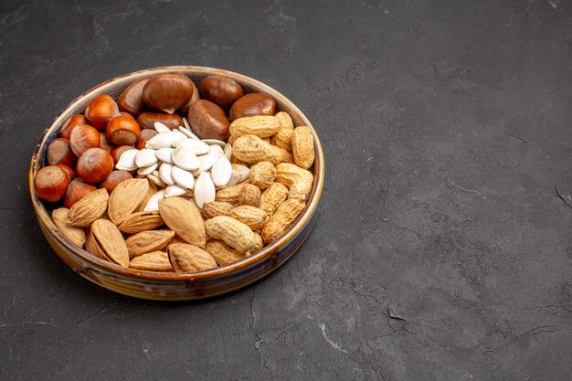 Vista frontal de diferentes nueces frescas, avellanas y otras nueces sobre superficie oscura