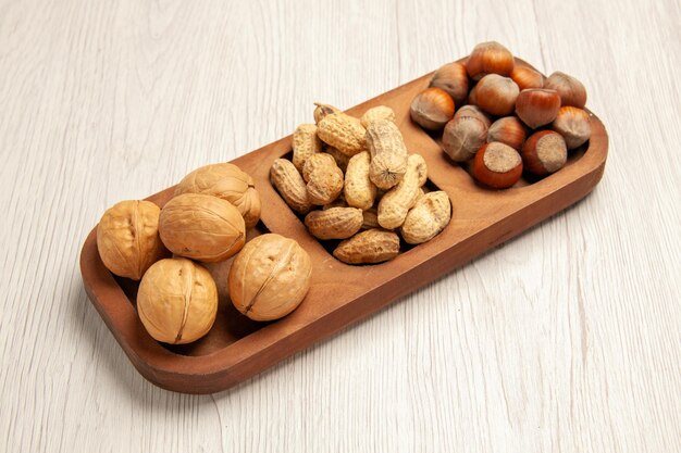 Vista frontal diferentes nueces frescas cacahuetes avellanas y nueces en el escritorio blanco tuerca snack muchas plantas