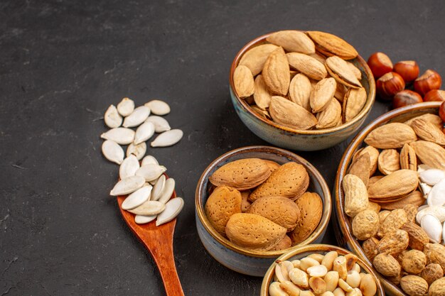 Vista frontal de diferentes nueces nueces frescas dentro de macetas en superficie oscura