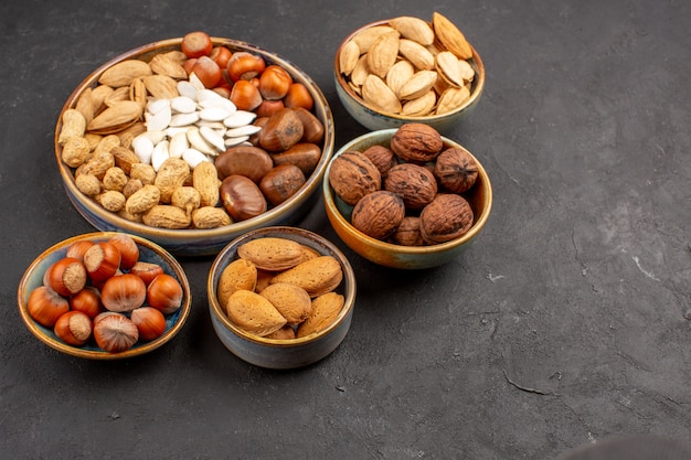 Vista frontal de diferentes nueces nueces frescas dentro de macetas en superficie oscura